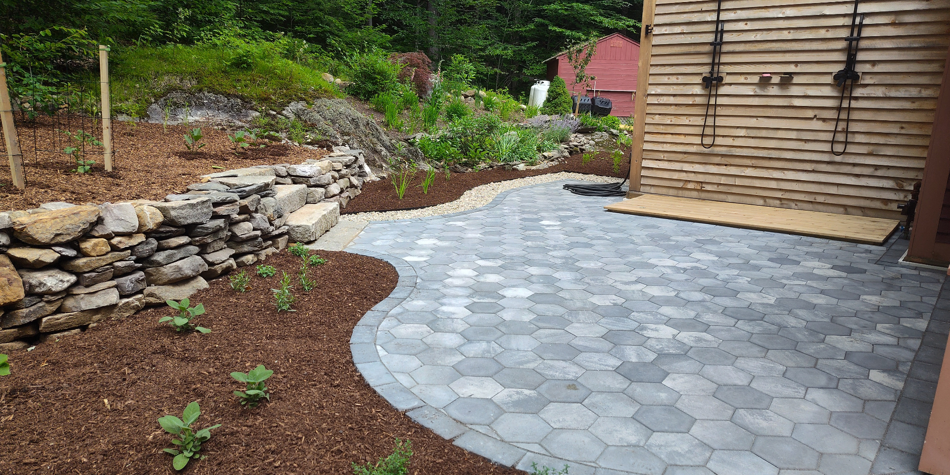 Stone patio with wooden chairs and a stone fire ring at the edge of a New Hampshire woodland