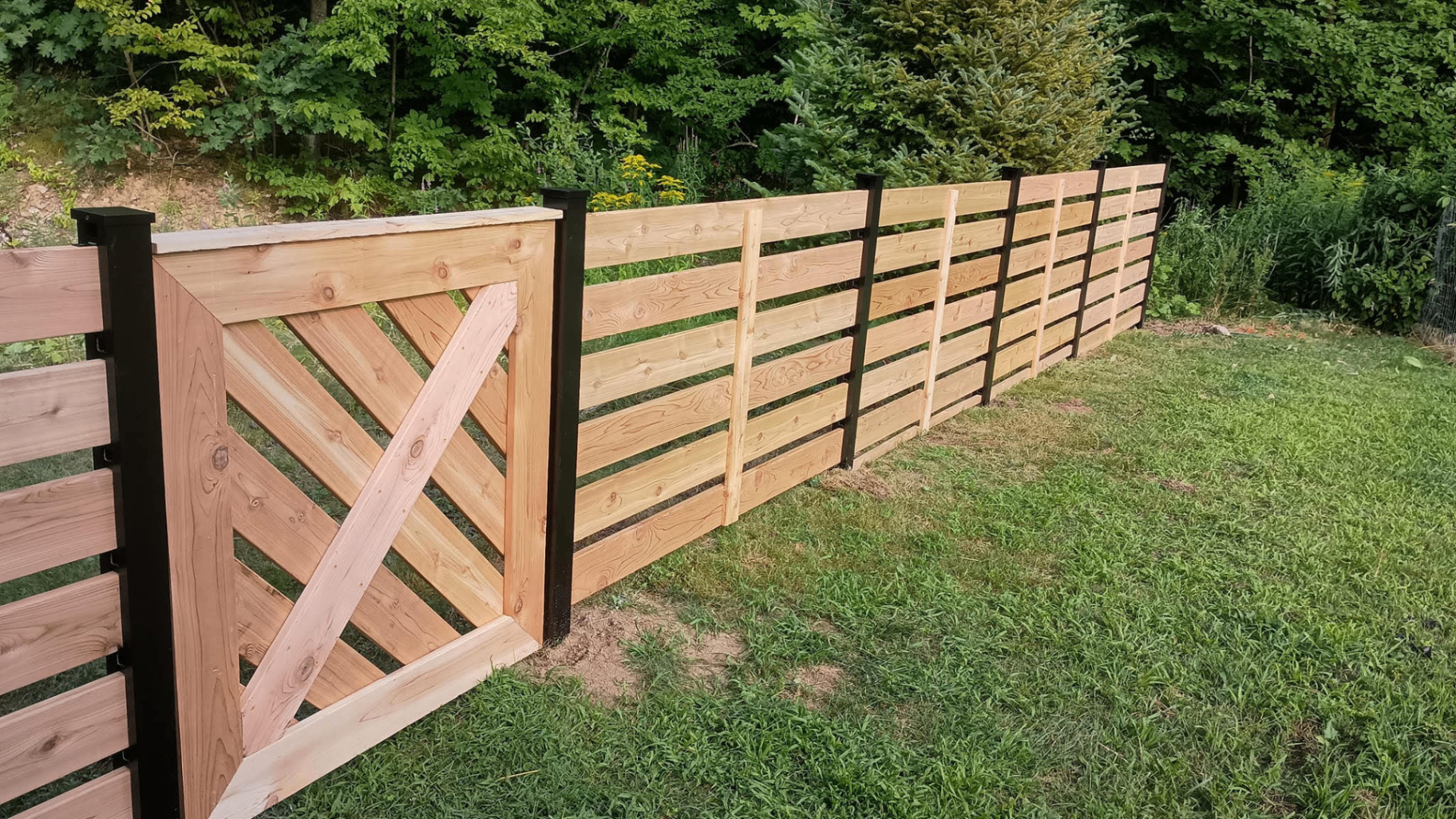 A custom cedar and steel horizontal-slat fence with a matching gate along a wooded property edge